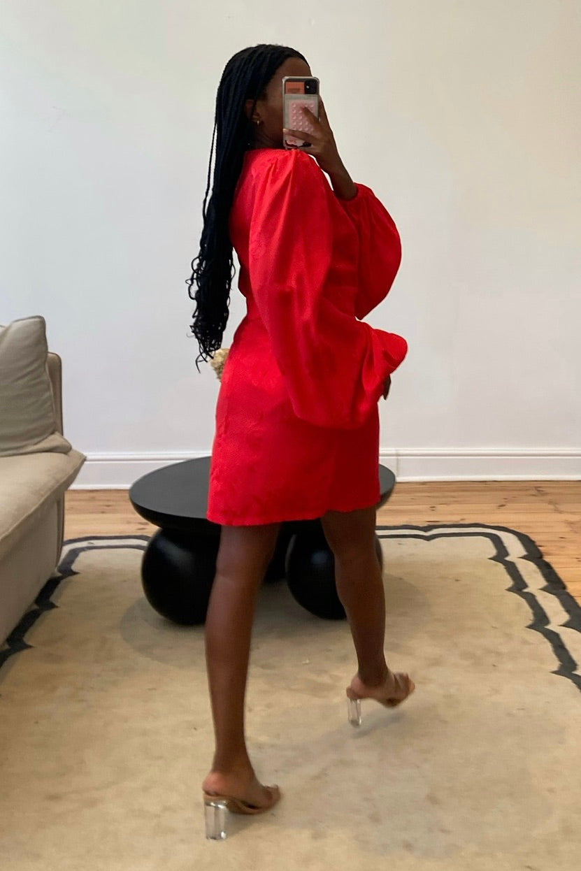 A person wearing a red long sleeve sheer style self-tie wrap dress with a deep v neckline and centre back zip closure.