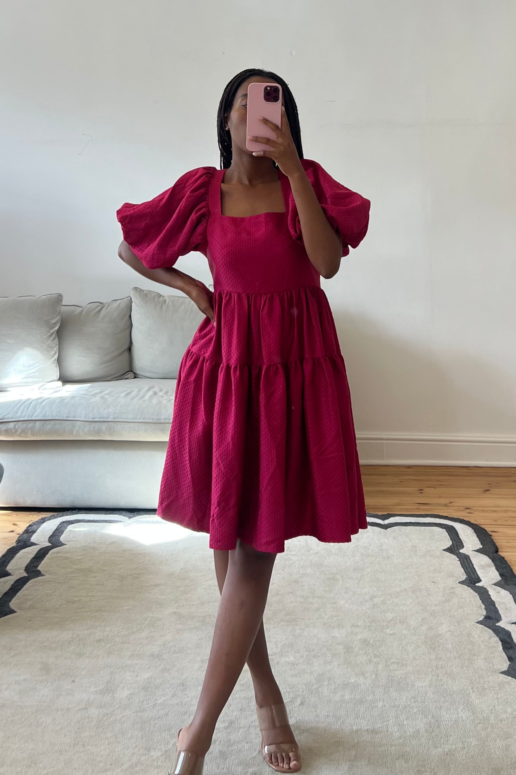Person wearing a pink dress taking a mirror selfie in a room with a couch and rug.