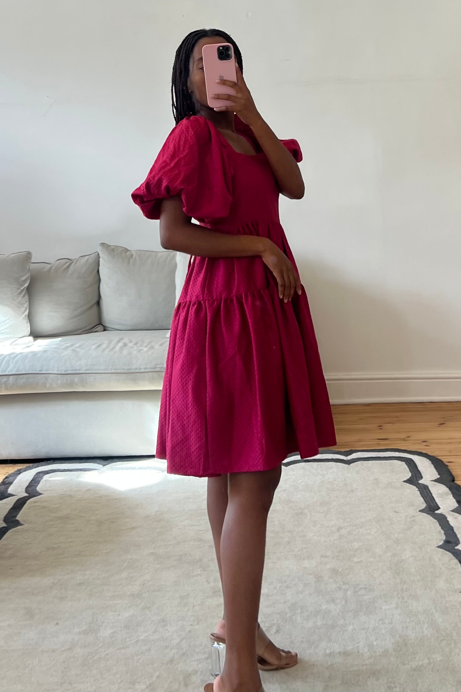 Person wearing a red dress taking a mirror selfie in a living room.