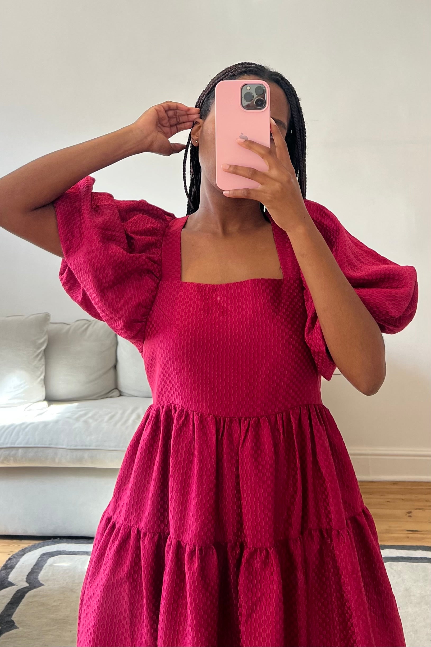 Person wearing a red dress taking a mirror selfie in a room with a couch and pillows.