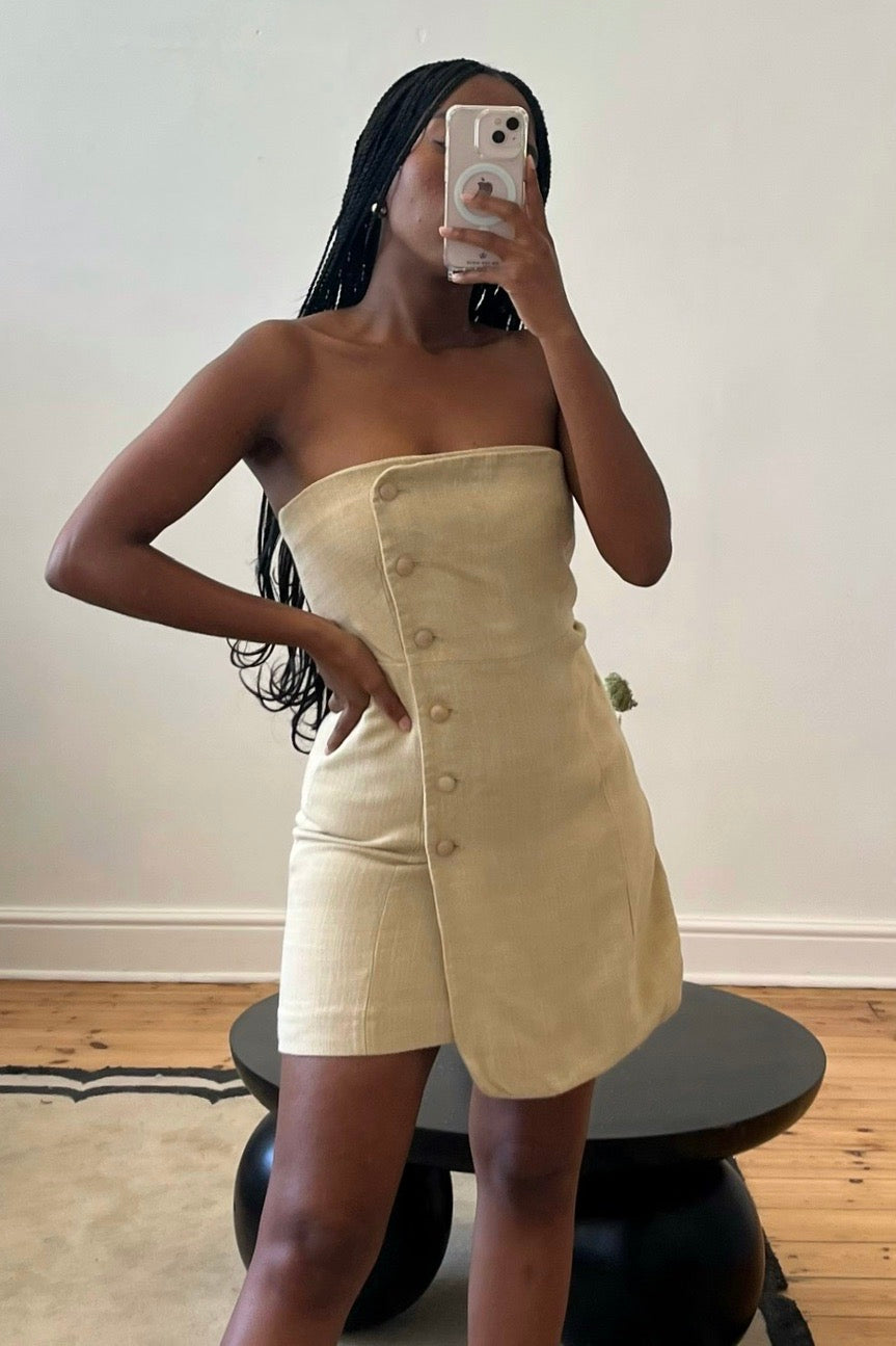 A person wearing a beige mini dress with a button front placket and smock detail at the back, made from 100% viscose fabric.