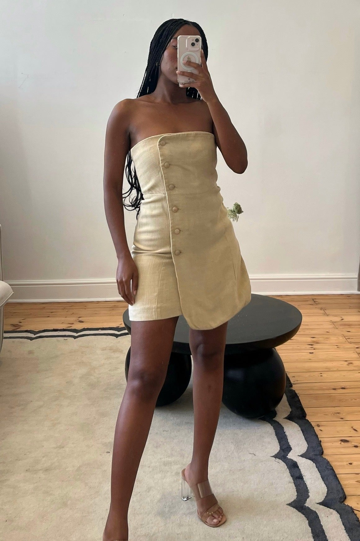 A person wearing a beige mini dress with a button front placket and smock detail at the back, made from 100% viscose fabric.
