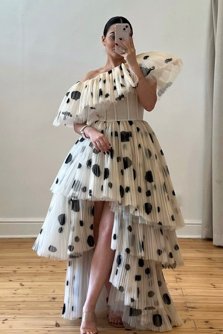 The Bradshaw Gown – a dramatic off-the-shoulder gown with micro pleats and a tiered skirt, perfect for formal occasions. Elegant, timeless, and available now.