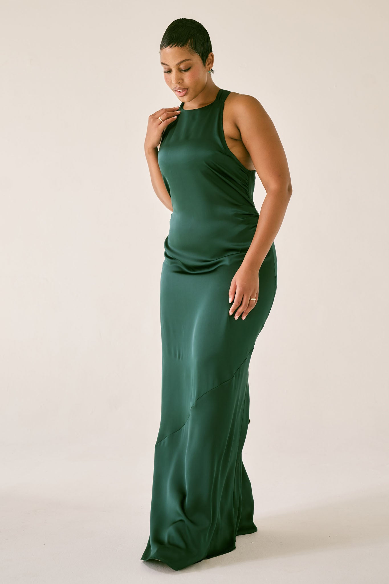 Woman in a sleeveless emerald green gown posing against a light background, suitable for weddings and formal events.
