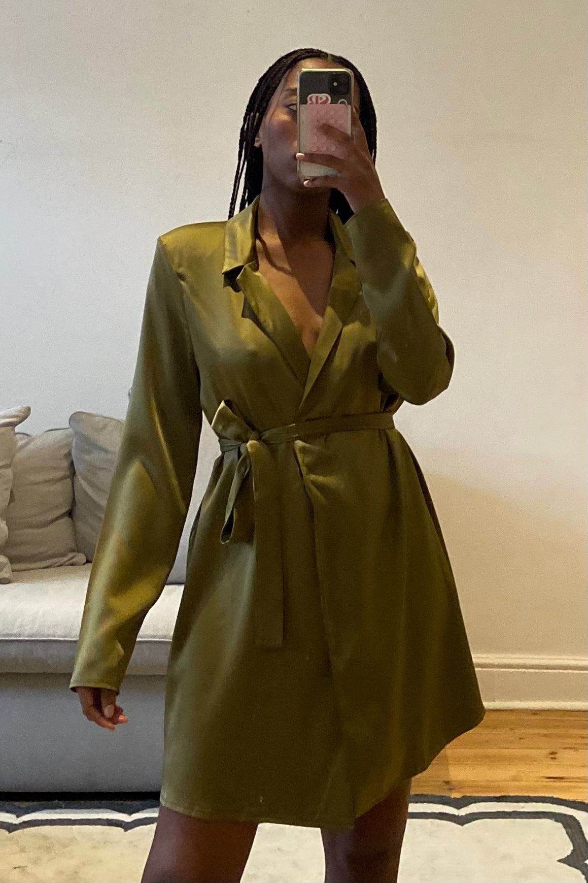 Person wearing a green dress taking a mirror selfie in a room with a couch and pillows.