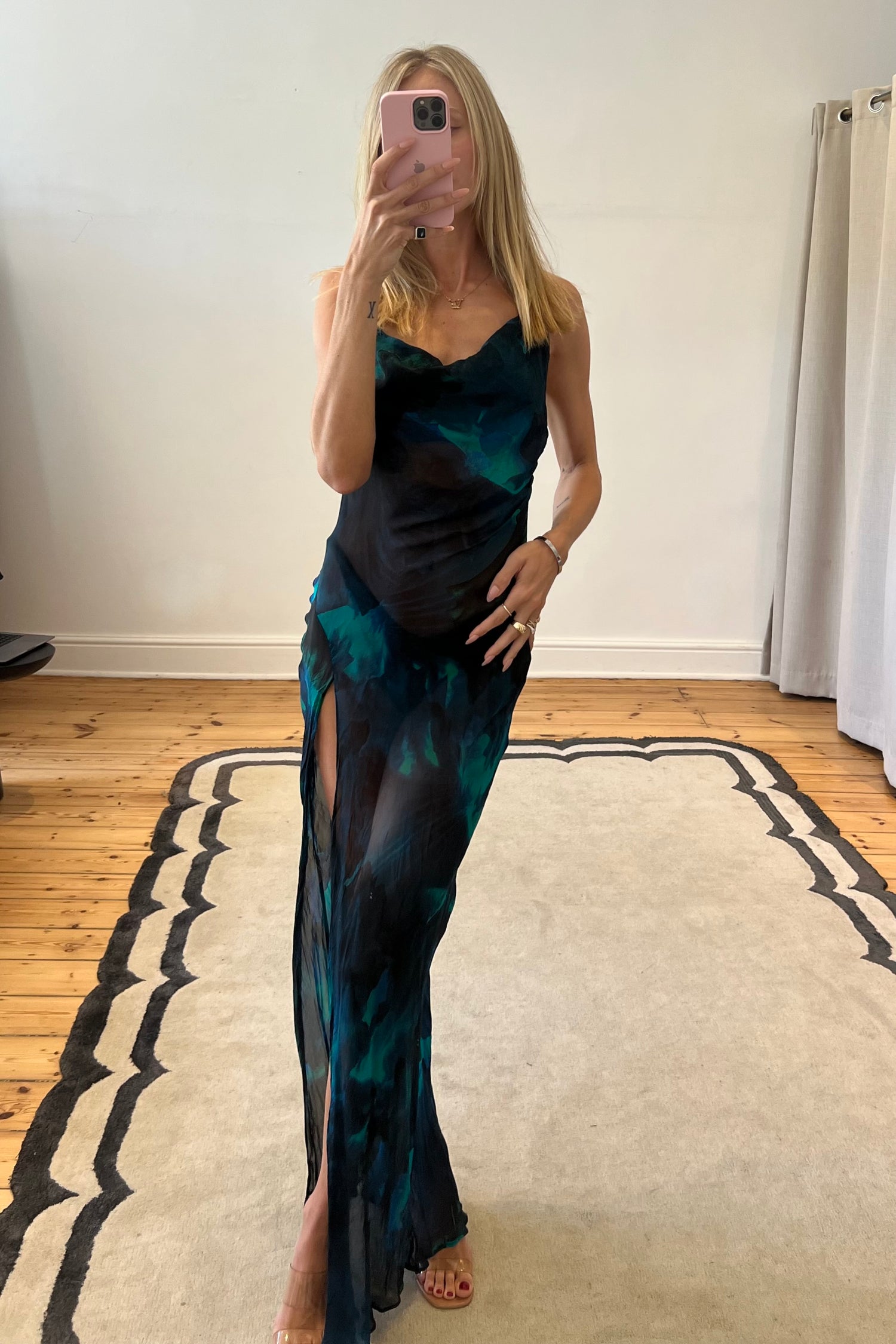 Woman taking a mirror selfie wearing a long, dark green patterned dress with a high slit.