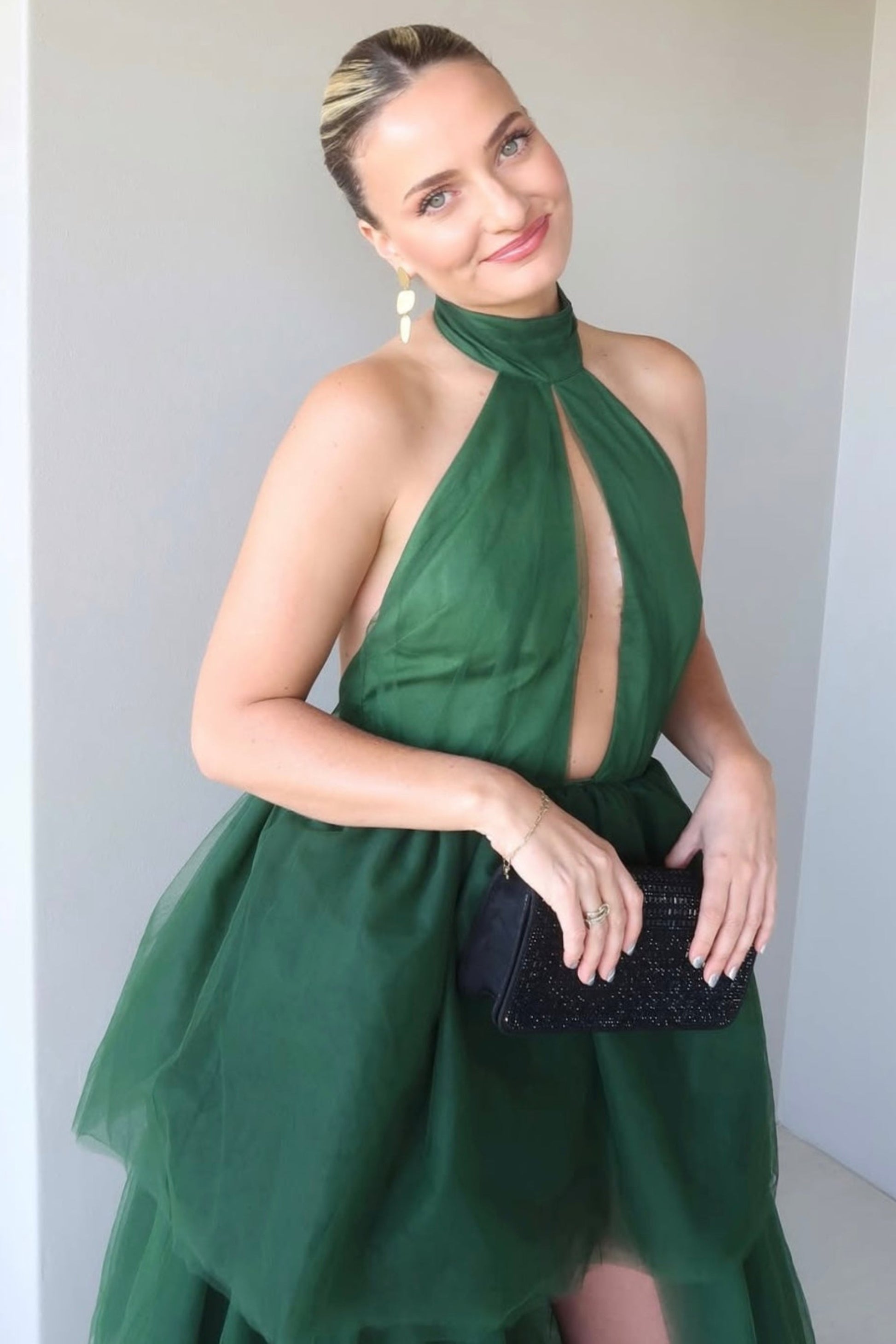 Woman wearing a green dress with a black clutch against a white background